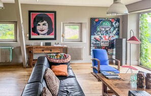 Un salon moderne avec un canapé en cuir noir, un fauteuil bleu, une table basse en bois et un grand tableau abstrait accroché au mur.
