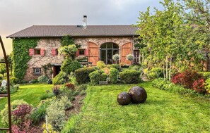 Une maison en pierre avec un jardin, une grande fenêtre et une porte.