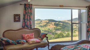 Una habitación con un amplio ventanal que ofrece vistas a ondulantes colinas y un pueblo lejano.