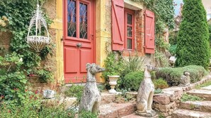 Un edificio rústico de piedra con contraventanas rojas, un farol colgante y una estatua de perro.