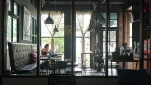 An interior with a large window, a bench, and a table with a person working on a laptop. - AO Apartment (Vientiane)