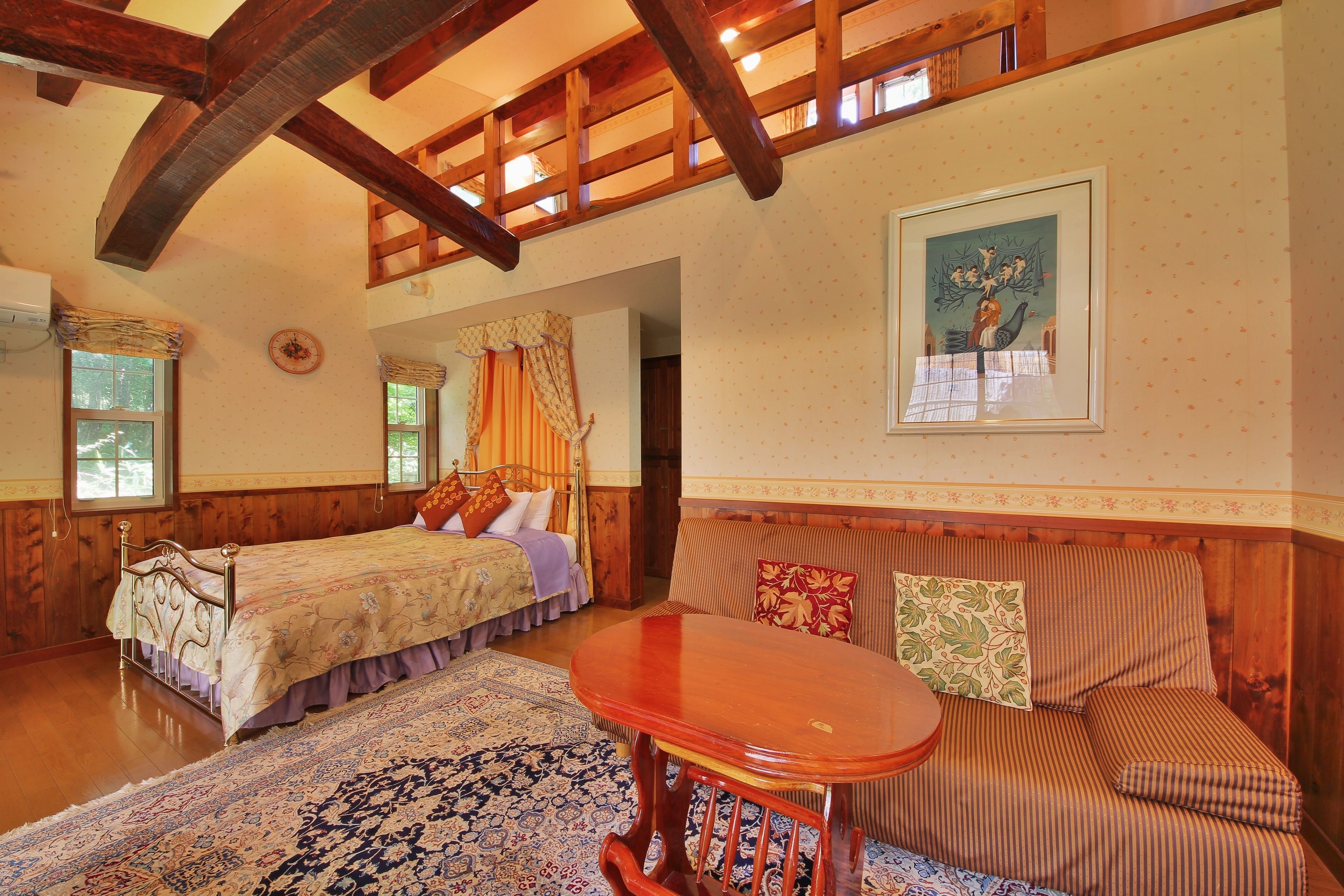 A cozy room with a wooden ceiling, a bed with a floral bedspread, a sofa with striped cushions, and a round wooden table.