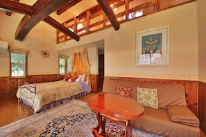 A cozy room with a wooden ceiling, a bed with a floral bedspread, a sofa with striped cushions, and a round wooden table. - One More Time (Nikko)
