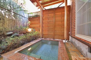 A rectangular hot tub with a stone border, surrounded by a wooden fence and a bamboo wall. - One More Time (Nikko)