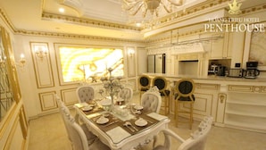 A luxurious penthouse dining area with a large table set for four, elegant chairs, a chandelier, and a modern kitchen with a marble backsplash. - Hoang Trieu Hotel (Ho Chi Minh City)