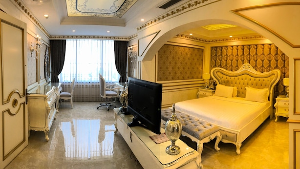 A luxurious hotel room with a large bed, a television, a desk with a computer, and a seating area with a chair and a table. - Hoang Trieu Hotel (Ho Chi Minh City)