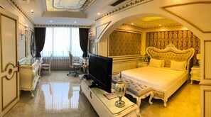 Une chambre d’hôtel luxueuse, dotée d’un grand lit, d’une télévision, d’un bureau avec un ordinateur et d’un coin salon comprenant un fauteuil et une table.