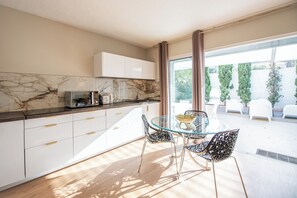 A modern kitchen with marble countertops, white cabinets, and a glass dining table with metal chairs.