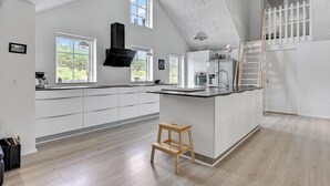 Una cocina moderna con armarios blancos, un taburete de madera y una campana extractora negra.