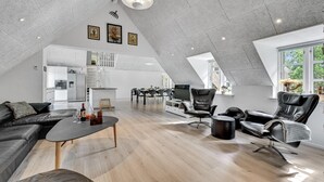 Amplio loft con techo alto, espacio con cocina, comedor y zona de estar con sillones y sofá de cuero.