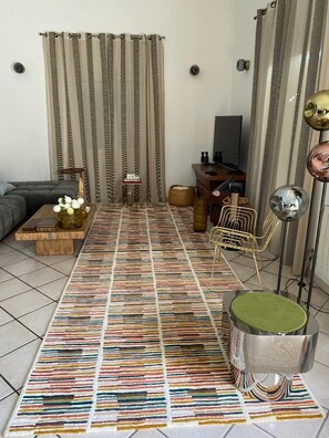 Ein Wohnzimmer mit Teppichmuster, einer Couch, einem Couchtisch mit Dekoration, einem Fernseher und einer Stehlampe.