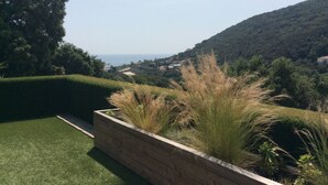 Ein angelegter Garten mit einem Holz-Pflanzbeet, einem gepflegten Rasen und Blick auf einen Hügel mit Gebäuden in der Ferne.