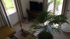 Ein Wohnzimmer mit einer Couch, einem Couchtisch mit Pflanze, einem Fernseher und einem Fenster mit Vorhängen.