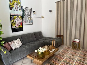 Una sala de estar con un sofá gris, una mesa de centro con objetos decorativos, una lámpara de pared y cortinas a rayas.