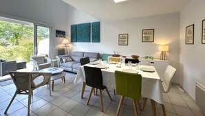 A dining area with a table set for four, a sofa, and a window with a view of greenery. - 3-bedroom vacation home with heated pool 6 beds (L'Aiguillon-sur-Vie)