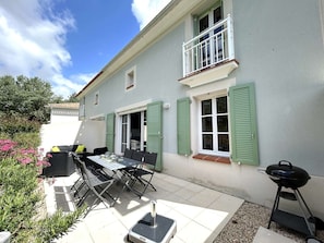 Une maison à deux étages dotée d’un patio comprenant une table et des chaises, un barbecue et un petit balcon.