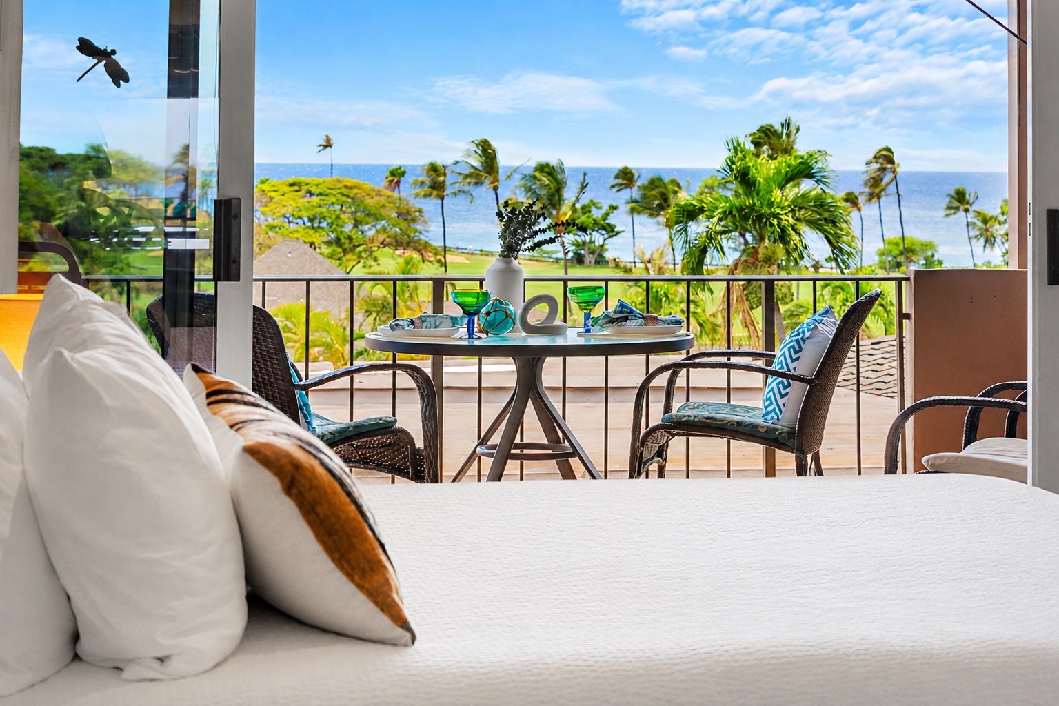 Een balkon met uitzicht op de oceaan, voorzien van een tafel, stoelen en een bed met kussens.
