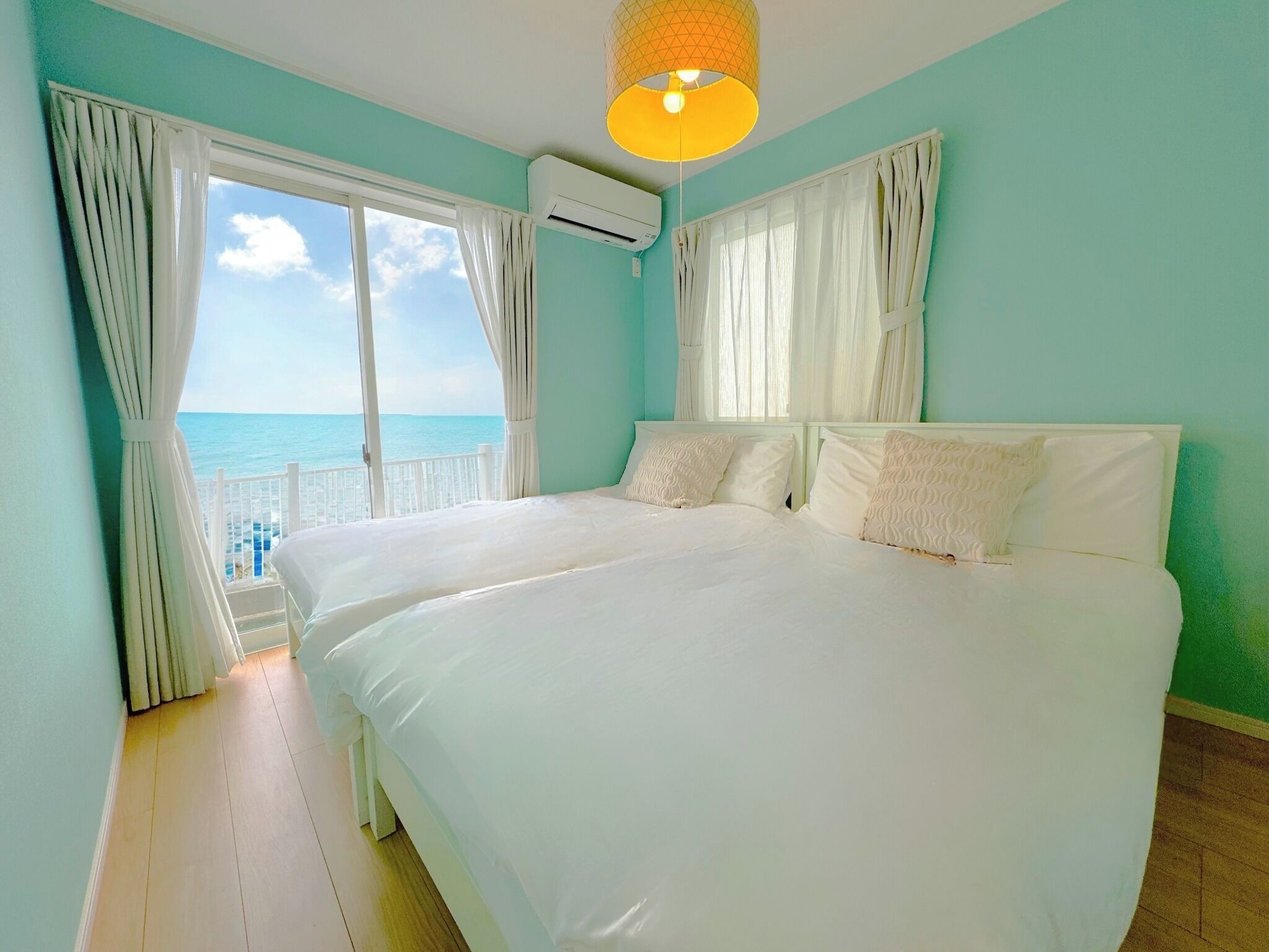 A bedroom with a large bed, white curtains, and a view of the ocean.