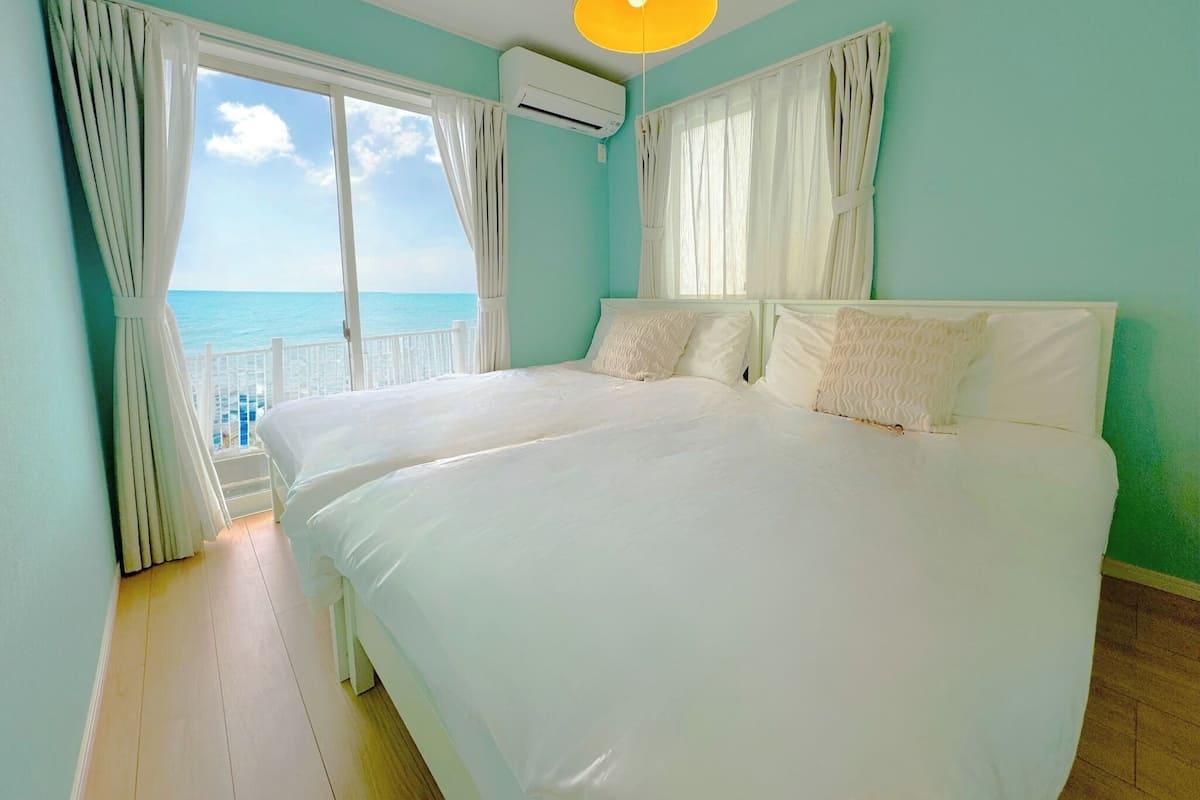 A bedroom with a large bed, white curtains, and a view of the ocean.