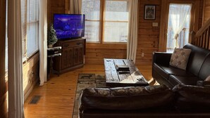 A cozy log cabin interior with a wooden floor, a leather sofa, a coffee table, a television, and a fireplace. - A Little Bit of Heaven. Hot tub, Pool Table, Pigeon Forge Cabin (Sevierville)