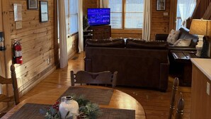 A cozy cabin interior with a wooden ceiling, a fireplace, a dining area with a table set for two, and a living room with a sofa and television. - A Little Bit of Heaven. Hot tub, Pool Table, Pigeon Forge Cabin (Sevierville)
