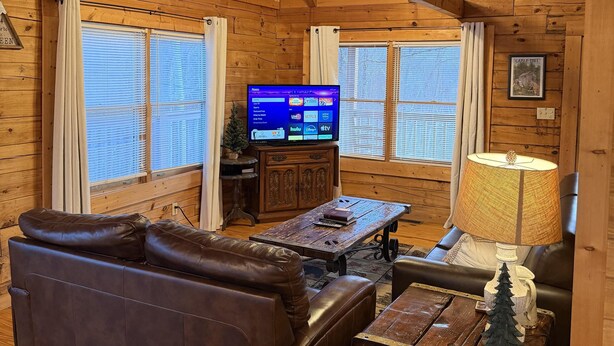 A cozy cabin interior with a wooden ceiling, a leather sofa, a wooden coffee table, and a television on a cabinet. - A Little Bit of Heaven. Hot tub, Pool Table, Pigeon Forge Cabin (Sevierville)