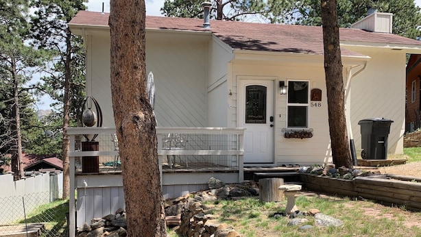 A single-story house with a white exterior, a front porch, and a mailbox. - Mountain Views,Downtown,RMNP,Fenced Backyard,Pet Friendly,Hot Tub!Woods&Waves (Estes Park)