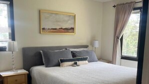 A bedroom with a bed, a nightstand, a ceiling fan, a window with curtains, and a painting on the wall. - Mountain Views,Downtown,RMNP,Fenced Backyard,Pet Friendly,Hot Tub!Woods&Waves (Estes Park)