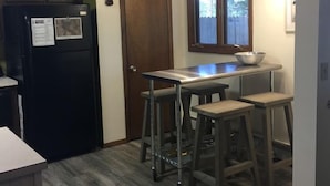 A compact kitchen with a refrigerator, a wooden door, a window, and a dining area with stools. - Mountain Views,Downtown,RMNP,Fenced Backyard,Pet Friendly,Hot Tub!Woods&Waves (Estes Park)