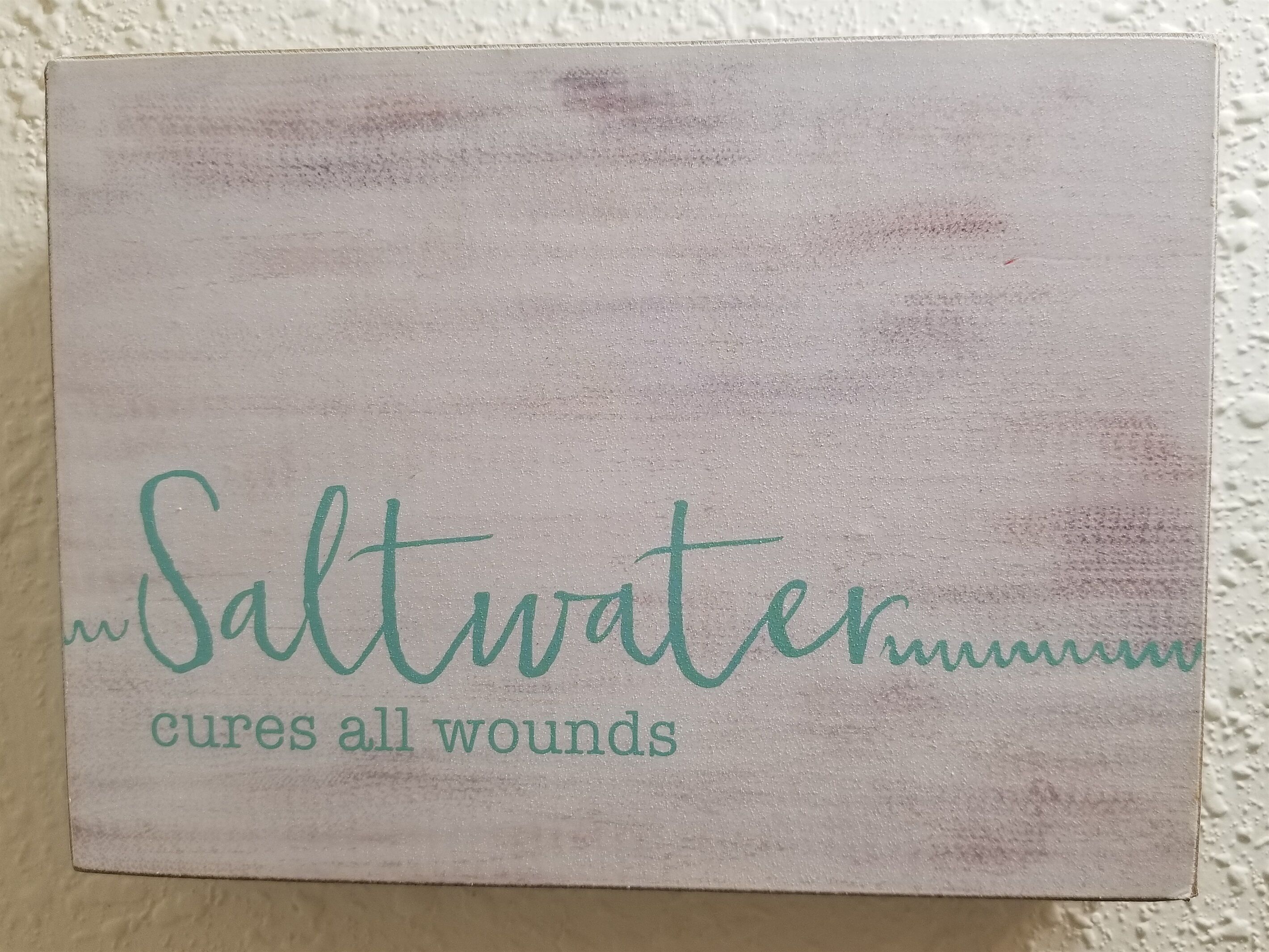 A sign with the text "Saltwater cures all wounds" on a textured wall.