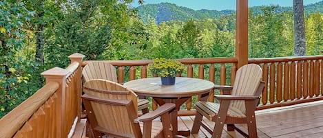 Een houten terras met een ronde tafel en vier Adirondack-stoelen, omgeven door een houten reling.