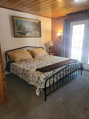 A bedroom with a bed, a painting on the wall, a lamp, and a window.