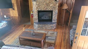 A cozy living room with a stone fireplace, wooden flooring, a sofa, and a coffee table. - Cozy Mountain Retreat / Great For Reunions, Family Retreats,  Room For Tents! (Duck Creek Village)