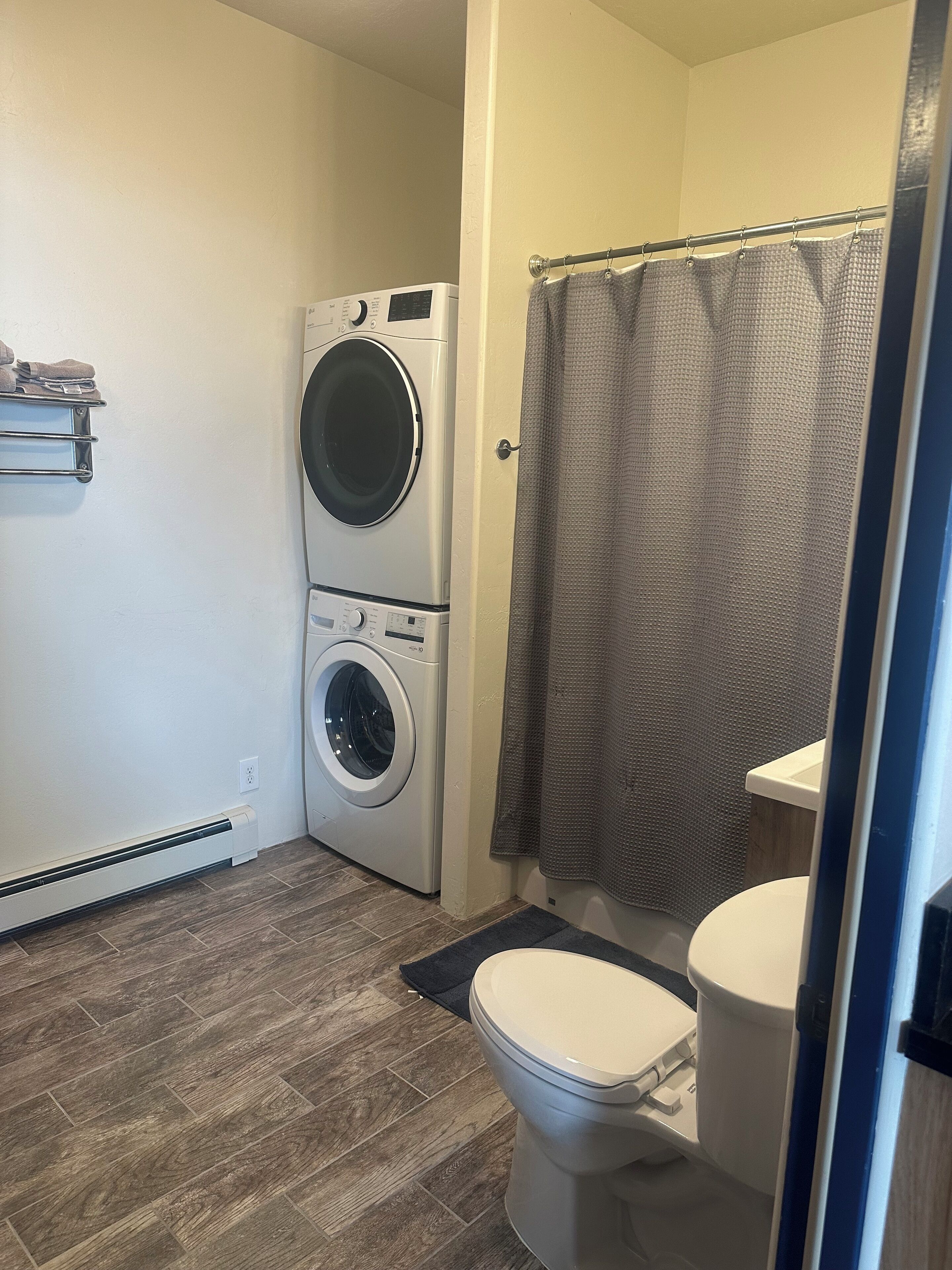A compact bathroom with a front-loading washer, a toilet, and a shower curtain.