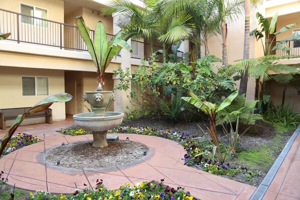 Un patio central con una fuente, rodeado de plantas y flores diversas.