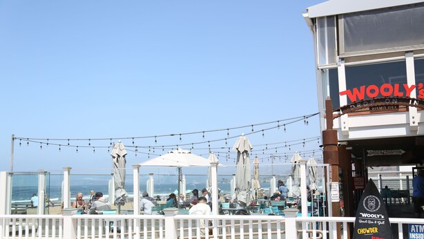 A beachside restaurant with outdoor seating, a clear view of the ocean, and a sign for Woolly's Drop on Pismo Beach, CA. - 2 Blocks to Ocean - Fall & Winter Special- Gated Building - 5 star reviews (Pismo Beach)