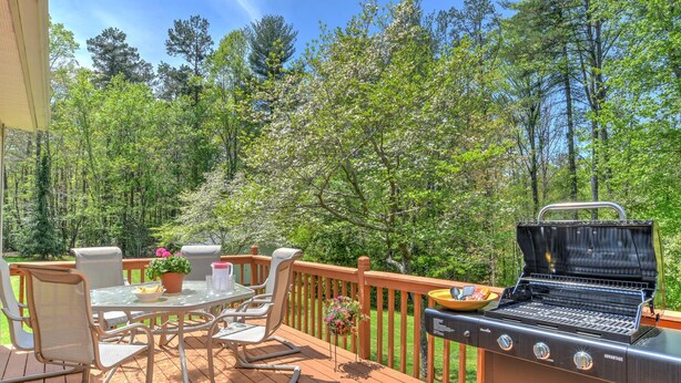 A deck with outdoor furniture, a grill, and a view of a forest. - Convenient and spacious 3 br, 1 sofa bed, 2 bath, lg yd, firepit, & patio area. (Asheville)