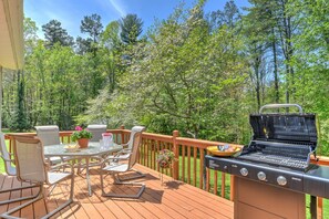 A deck with outdoor furniture, a grill, and a view of a forest.
