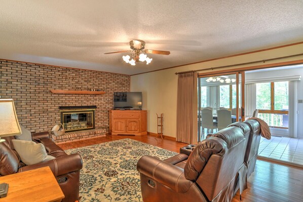 A living room with a brick fireplace, leather sofas, a TV, and a dining area with a view.