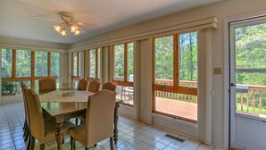A dining room with a large table and chairs, large windows, and a ceiling fan. - Convenient and spacious 3 br, 1 sofa bed, 2 bath, lg yd, firepit, & patio area. (Asheville)
