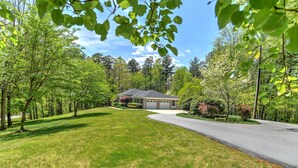 A residential property with a well-maintained lawn, a driveway leading to a garage, and a variety of trees and shrubs. - Convenient and spacious 3 br, 1 sofa bed, 2 bath, lg yd, firepit, & patio area. (Asheville)