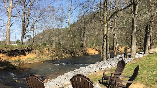 Una riva del fiume con sedie rivolte verso l'acqua, circondata da alberi e da una sponda rocciosa.