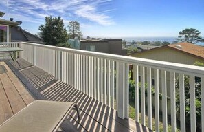 Una terraza de madera con barandilla blanca, con vistas a una zona residencial con casas y árboles.