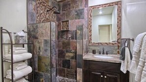Un bagno con cabina doccia in pietra, porta asciugamani in vetro, lavabo con specchio e mobili contenitori in legno scuro.