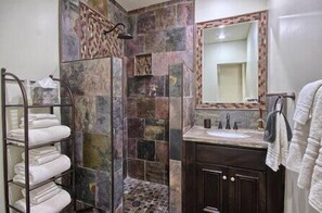 Un baño con cabina de ducha de piedra, toallero de vidrio, lavabo con espejo y armarios de madera oscura.