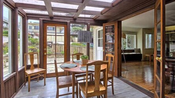 Une véranda avec un plancher en bois, une table entourée de chaises et de grandes fenêtres.