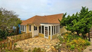 Une maison à deux étages avec une terrasse en pierre, une clôture en bois et un grand arbre.