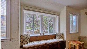 Une pièce avec un banc intégré sous une grande fenêtre, une petite table et un radiateur fixé au mur.