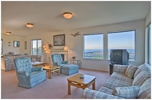 Relax in this inviting living room with a plush sofa, armchair, and fireplace, perfect for unwinding and enjoying the view.