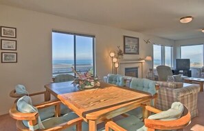 Enjoy a warm gathering around the fireplace in this inviting living room with a large dining table and ocean views.